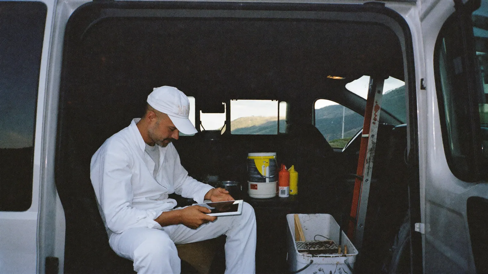 Maler in Arbeitskleidung sitzt im Lieferwagen und schaut auf ein Tablet